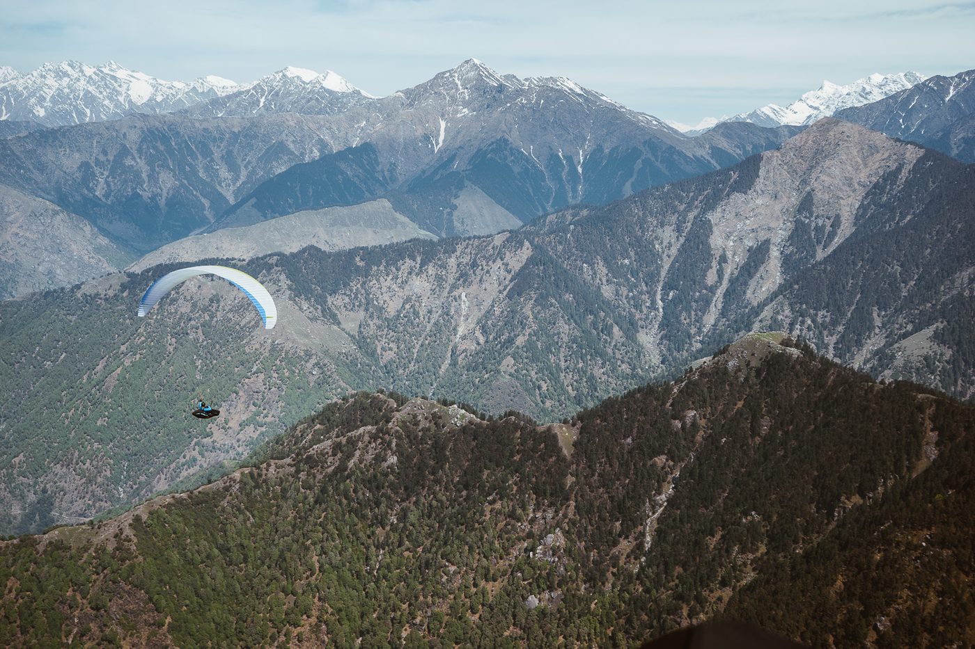 A pilot flying along the forested front range, snow peaks behind