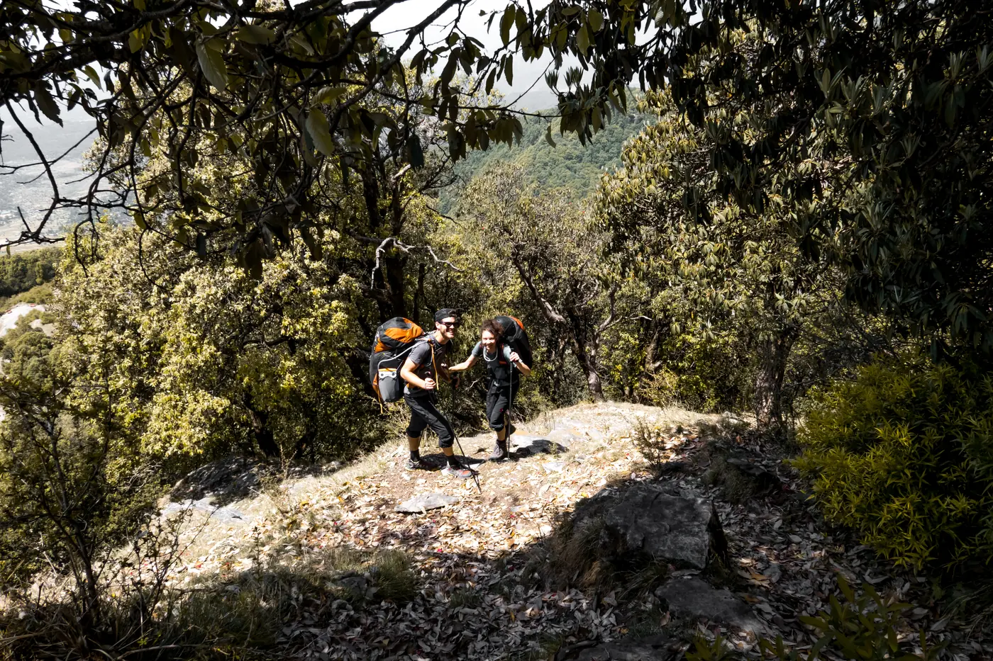 Two pilots with paraglider rucksacks climbing a forest trail