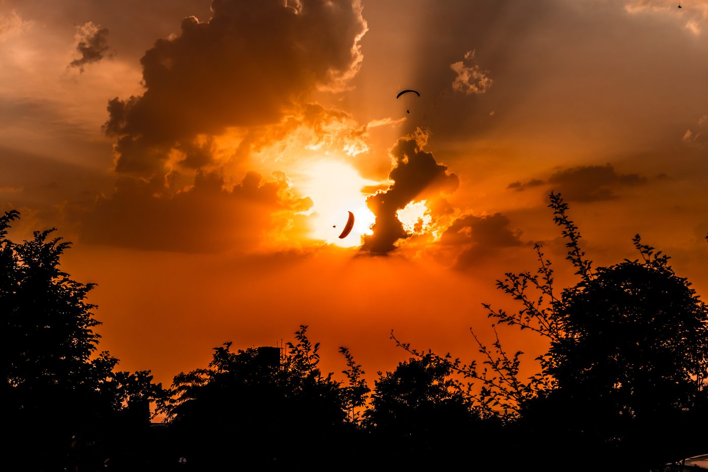 A paraglider silhouetted against a burning sunset