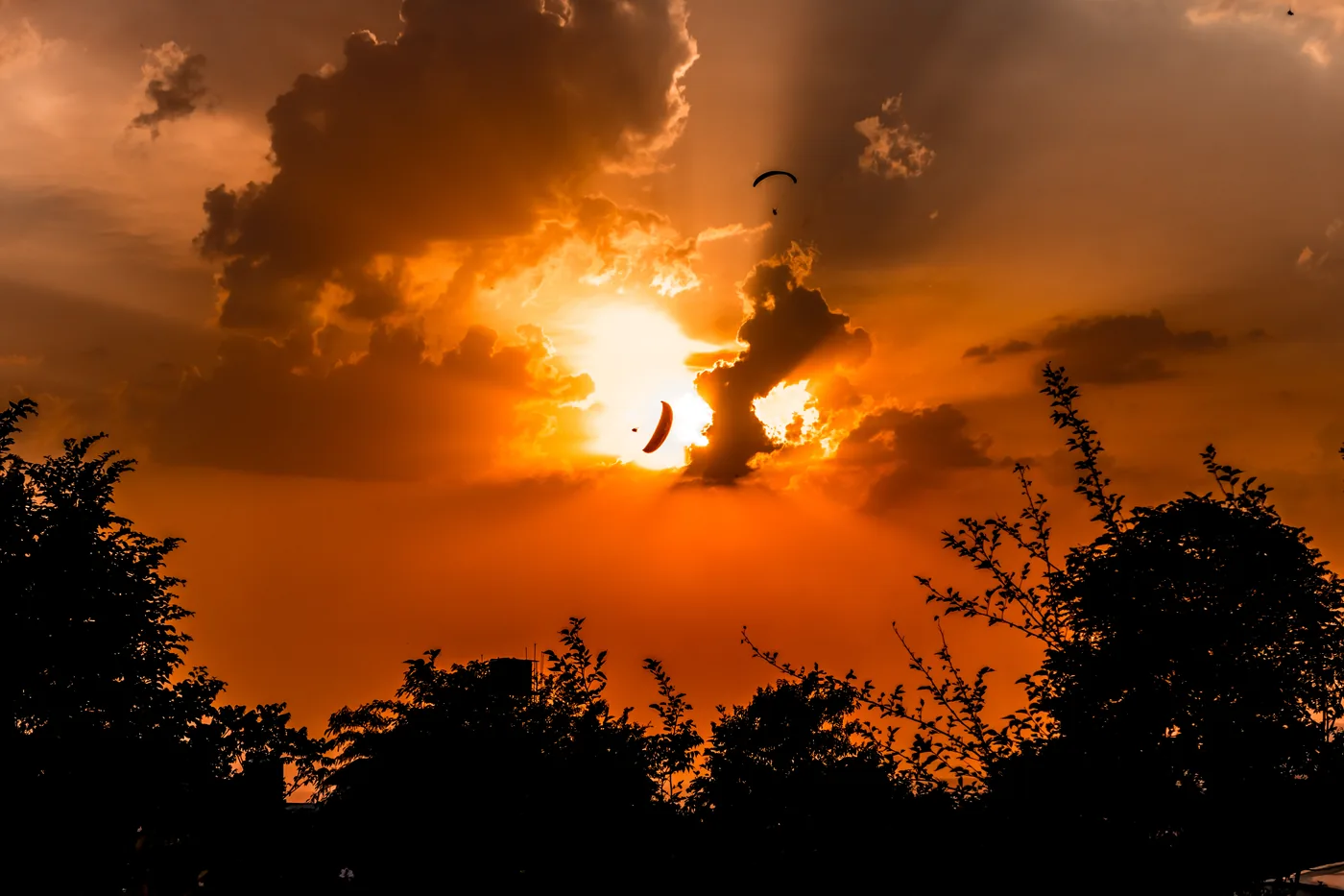 A paraglider silhouetted against a burning sunset