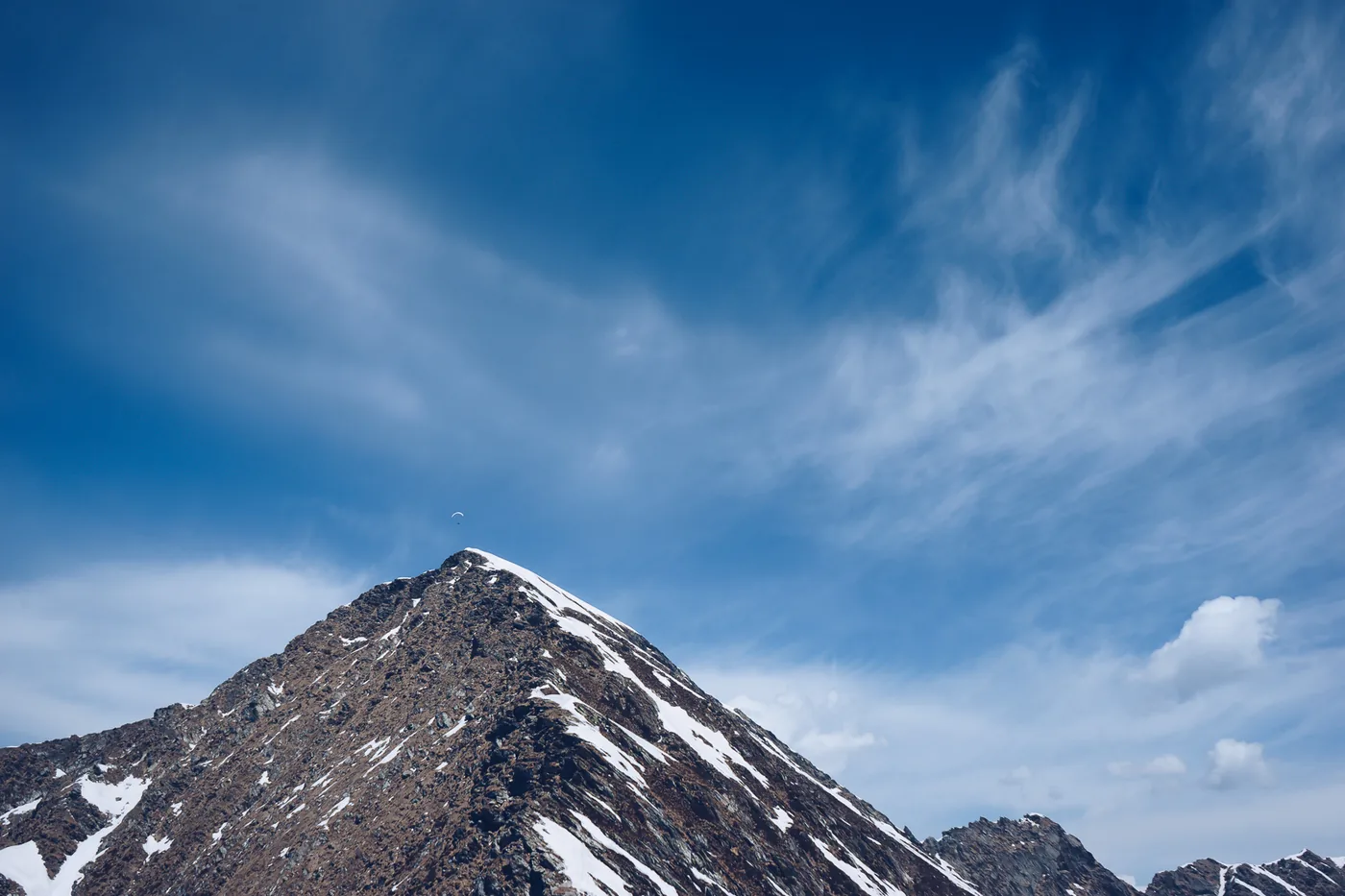A single wing high above a snow-streaked peak