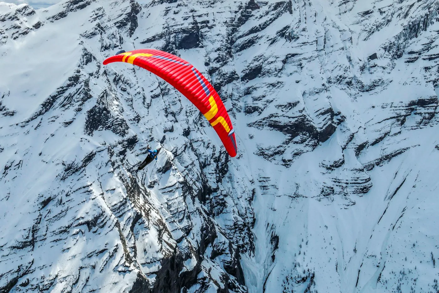 A pilot on a red wing turning over steep snow