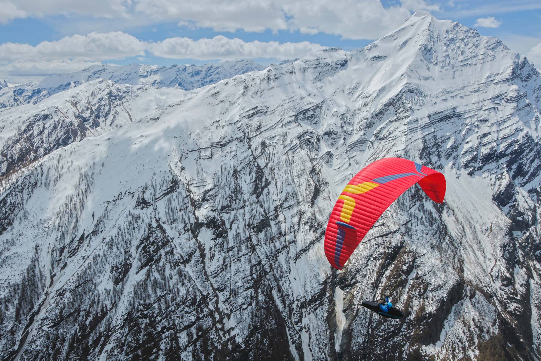 A pilot on a red wing flying over snow-covered mountains
