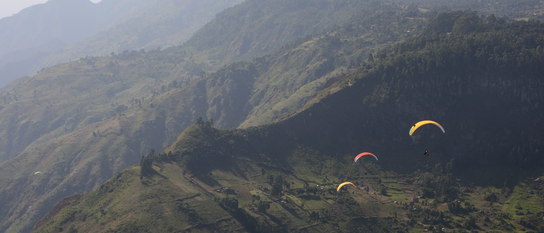 Three wings crossing a green ridgeline toward distant hills