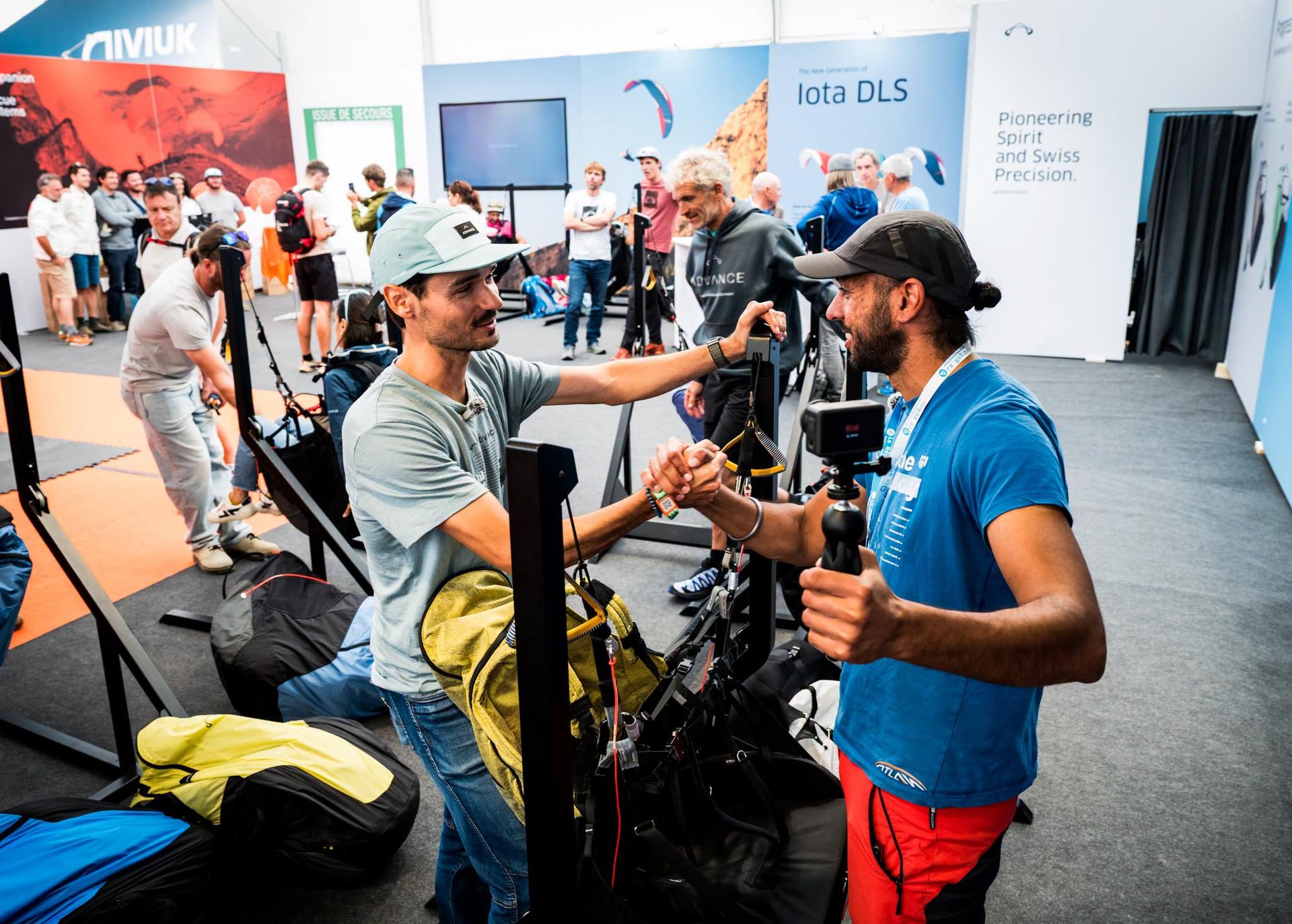 Aninder shaking hands with a brand representative at a harness test stand, camera in hand, at Coupe Icare